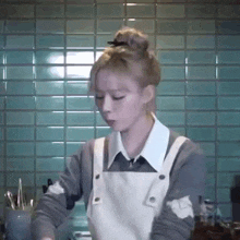 a woman in an apron is cooking in a kitchen with a bun in her hair .
