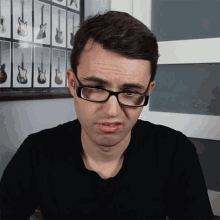 a man wearing glasses is making a funny face in front of a wall of guitars