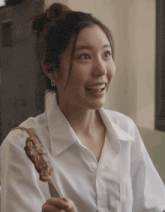 a woman in a white shirt is holding a skewer of meat