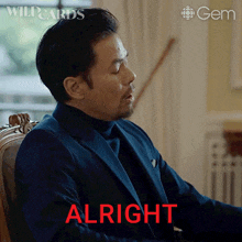 a man in a suit is sitting in a chair and the word alright is on the screen