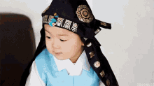 a baby wearing a black hat and a blue vest is sitting on a couch .