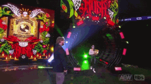 a man in a suit stands in front of a large screen that says aew tbs
