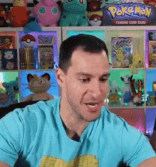 a man in a blue shirt is sitting in front of a shelf filled with pokemon toys .