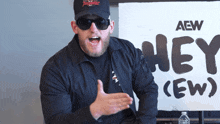 a man wearing sunglasses stands in front of a sign that says hey
