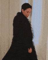 a woman in a black coat is standing in front of a white curtain