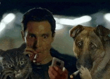 a man is smoking a cigarette next to a dog and a cat while holding a cell phone .