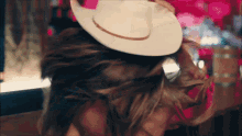 a woman wearing a white cowboy hat is dancing with her hair blowing in the wind