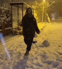 a person is walking in the snow at night while holding a bag .