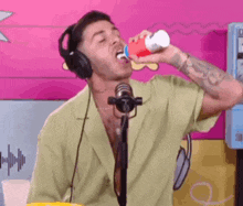a man wearing headphones is drinking from a bottle while standing in front of a microphone .