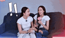 two women are sitting on a couch and one is holding a microphone that says ' vogue ' on it