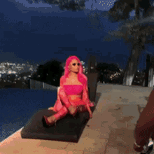 a woman with pink hair is sitting on a chair by a pool