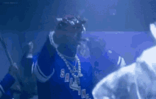 snoop dogg is wearing a blue jersey and holding a stick in a crowd of people .