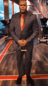 a man in a suit and tie is standing on a wooden floor with his hands folded .