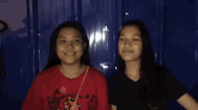 two women are sitting next to each other in front of a blue wall and making funny faces .