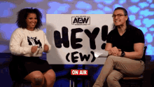 two people are sitting in front of a sign that says hey ( ew )