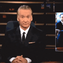 a man in a suit and tie is sitting in front of a screen