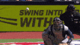 a catcher catches a baseball in front of a sign that says swing into with