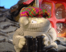 a stuffed animal wearing a sweater and a hat looks through binoculars