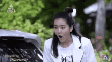 a woman is standing next to a car with her mouth open and a surprised look on her face .