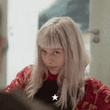 a girl with blonde hair and a red jacket has a star on her chest