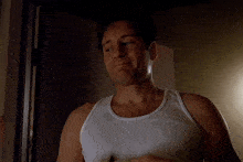 a man wearing a white tank top is standing in a dark room