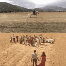 a group of people are dancing in a field while a man rides a horse in the background