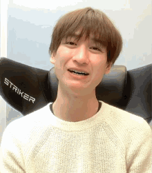 a man wearing a white sweater is sitting in a striker gaming chair