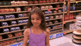 a girl in a purple tank top stands in front of a display of bread
