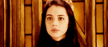 a woman wearing a tiara and a black dress is looking at the camera .