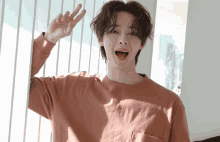 a young man wearing a pink shirt is waving his hand