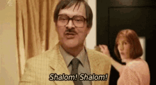a man in a suit and tie is standing next to a woman and saying shalom ! shalom ! .