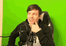 a young man wearing headphones and a shirt that says techno tour is sitting in front of a green screen