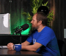 a man in a blue shirt is sitting at a table in front of a microphone with a cup that says bet on it