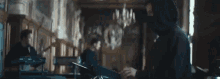 a man in a hooded jacket is playing a piano in a room with other people .