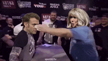 a woman is pointing at a man in front of a sign that says ' abtna ' on it