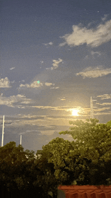 a full moon shines brightly in a cloudy sky above trees