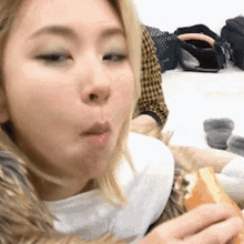 a woman is eating a sandwich and making a funny face while sitting on the floor .