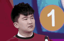 a young man in a red sweater is standing in front of a circle with the number one on it .