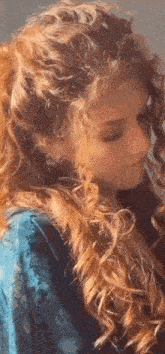a woman with long red curly hair is wearing a blue dress and looking down .