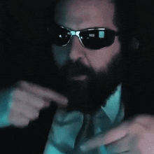 a man with a beard wearing sunglasses and a tie .