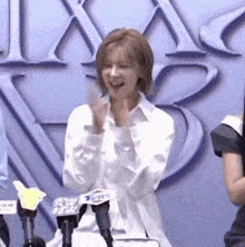 a woman in a white shirt is sitting in front of a microphone and clapping her hands .