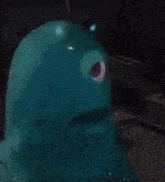 a blue monster with a red eye is sitting on a table in a dark room .