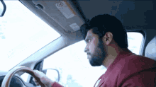 a man in a red shirt is driving a car with a warning sign on the visor