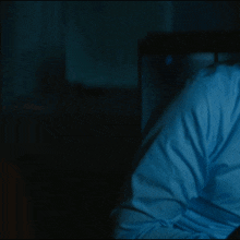 a person in a blue shirt is sitting in a dark room