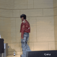 a man in a red jacket and jeans stands in front of a wall