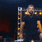 a man with a beard wearing a black shirt and a necklace is standing in front of a stage .