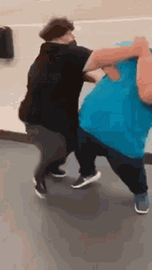 two people are fighting in a gym and one is wearing a blue shirt .