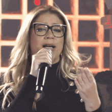 a woman singing into a microphone with glasses on