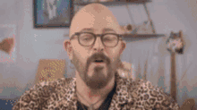 a bald man with glasses and a mustache is holding a remote control in front of a glass door .