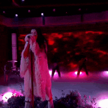 a woman singing into a microphone with a pink background